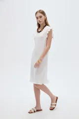 Vestido midi de poliéster color blanco, de corte recto y escote redondo a la base, con mangas cortas abuchonadas con volados y detalles de volados en el ruedo.