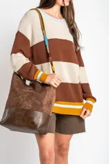 Bolso tipo shopper de tamaño maxi, confeccionado en material efecto gamuza marrón con base en cuero sintético oscuro. Cuenta con una correa ajustable y desmontable trenzada en varios colores.