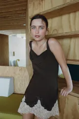 Vestido corto de viscosa color marrón chocolate, con escote fluido y tirantes anchos. Presenta un diseño asimétrico en el bajo con bordados y aplicación de encaje en color crema a contraste.