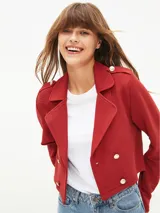 Chaqueta corta tipo blazer en color bordó, con diseño de doble botonadura frontal, solapas clásicas y detalles de charreteras en los hombros con botones metálicos.