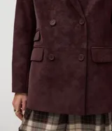 Blazer estructurado de corte sastre confeccionado en tejido sintético tipo gamuza (suede), con diseño de abotonado cruzado, solapas clásicas, bolsillos con tapa y mangas largas con botones en los puños.