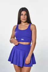 Conjunto deportivo compuesto por un top corto de escote redondo con logo estampado y una pollera short con vuelo. Ambas piezas son de color violeta.