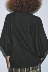 Jersey de punto liso color gris oscuro, con cuello redondo y mangas cortas anchas. Presenta terminaciones en rib en el cuello, puños y ruedo.