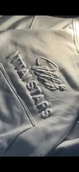 Hoodie de color blanco off-white con diseño de capucha, bolsillo frontal tipo canguro y bordado en relieve con el texto ITTAI STARS y un logo caligráfico.
