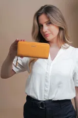 Billetera larga tipo sobre de la marca Lincoln's, confeccionada en material sintético con textura suave en color beige. Presenta un cierre perimetral metálico y el logo de la marca grabado en la parte frontal.