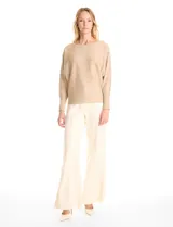 Buzo de tejido fino color beige, con mangas tipo dolman y puños ajustados. Presenta un diseño frontal decorado con apliques de tachas metálicas pequeñas dispuestas en líneas verticales.