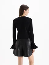Cardigan negro de tejido de punto semi liviano, con calce al cuerpo, escote redondo y cierre frontal con botones. Mangas largas con puños godet acampanados que aportan volumen.