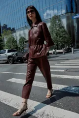 Chaqueta efecto piel color marrón, con cuello solapa, mangas por debajo del codo, cintura elástica, falsos bolsillos delanteros y cierre frontal con cremallera.