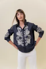 Camisa de denim liviano color azul oscuro con bordado artesanal en tono crudo en el frente y en las mangas. Presenta cuello clásico y cierre frontal con botones, con un calce relajado.