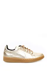Zapatilla deportiva clásica de cuero liso color dorado metalizado, con cordones beige y suela de goma color caramelo.