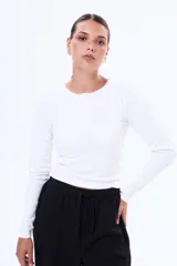 Remera de manga larga en tejido de punto acanalado, color blanco, con cuello redondo y cierre frontal parcial con botones.