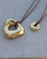 Collar con dije de forma irregular en tonos dorados y plateados, suspendido de un cordón doble de algodón negro.