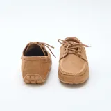 Mocasines náuticos de hombre en color tostado, confeccionados en material sintético con efecto gamuza. Presentan costuras visibles en relieve, cordones decorativos laterales y cierre frontal con cordones en el empeine.