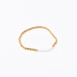 Pulsera elástica con cuentas doradas y cuentas facetadas blancas.
