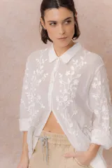 Camisa blanca de calce relajado con tejido semitransparente y bordados florales en relieve. Cuenta con cuello camisero, abotonadura frontal y mangas amplias.