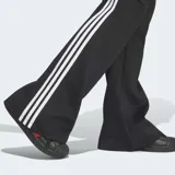 Pantalón acampanado Adidas de la colección Adicolor, color negro con las icónicas tres tiras blancas a los lados y el logo del trifolio bordado.