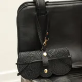 Estuche para lentes de ecocuero negro con textura granulada, diseño minimalista con cierre de broches metálicos dorados y correa de mano desmontable.