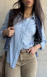 Camisa celeste de manga larga con bordados geométricos frontales a lo largo de la botonadura, cuello camisero clásico y cierre frontal de botones.