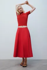 Falda midi de tiro alto y corte en A, color rojo, con bolsillos laterales ocultos y cierre lateral con cremallera.