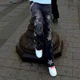 Jeans negros de corte flare con diseño de estrellas aplicadas en tono grisáceo y detalles desgastados con roturas en las piernas.