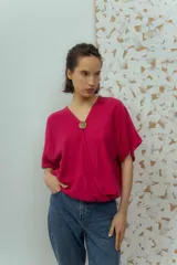 Blusa de lino color fucsia, con escote en V y manga corta amplia. Presenta un detalle de botón decorativo dorado en el centro del escote.
