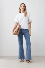 Blusa blanca de corte holgado con cuello redondo, mangas cortas con detalle de volados y ruedo con terminación de volado pequeño.