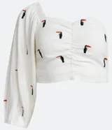 Blusa cropped de lino blanca con manga tres cuartos, hombro asimétrico, escote corazón, lastex en la espalda y bordados de tucanes.