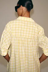 Vestido midi camisero de algodón, color amarillo con estampado a cuadros. Cuenta con cuello solapa, escote en V, mangas cortas con puño y bolsillos laterales ocultos en la costura, con diseño evasé.