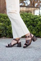 Sandalias de cuero color marrón chocolate con taco ancho, diseño de tiras cruzadas con textura símil serpiente y tira ajustable en el talón con hebilla metálica.