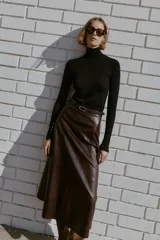 Jersey de punto liso en color beige, con cuello alto y manga larga con detalle de botones metálicos en los puños.