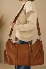 Bolso tipo Duffle color suela, confeccionado 100% en cuero vacuno, con asas de mano y correa larga ajustable y desmontable.