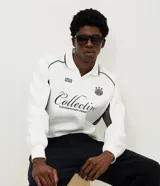 Buzo deportivo de felpa en color blanco con detalles en negro. Presenta cuello tipo polo, mangas largas con puños acanalados y diseño con recortes laterales. Incluye estampados gráficos en el frente con tipografía cursiva y emblema circular.