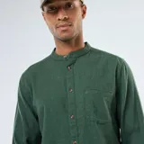 Camisa de manga larga de franela verde oscuro, con cuello mao y cierre frontal de botones marrones. Posee un bolsillo de parche en el pecho izquierdo.