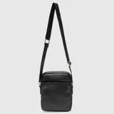 Bandolera de cuero sintético negro con diseño rectangular, cierre principal y bolsillo frontal con cierre. Incluye correa ajustable para llevar cruzada al hombro.