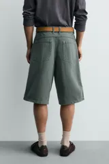 Bermuda tipo jorts de algodón color verde oscuro, con corte relajado y tiro medio. Presenta bolsillos frontales y bolsillos traseros de plastrón.