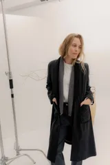 Tapado largo de corte recto y estilo minimalista, confeccionado en tela de color negro. Presenta solapas amplias, bolsillos frontales de parche y un diseño abierto que permite superponer capas.