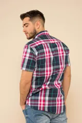 Camisa de manga corta con estampado de cuadros en tonos verdes, azules y blancos. Presenta cuello clásico, cierre frontal con botones y dos bolsillos delanteros con solapa.
