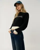 Buzo Rip Curl de punto color negro con diseño de bloques de color, presenta paneles en color crudo en los puños, cuello y el borde inferior. Incluye la inscripción "Rip Curl" bordada en el pecho con tipografía estilo gótico.