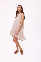 Vestido corto beige de lino, sin mangas, con escote redondo y detalle de abertura en forma de lágrima en el pecho. Presenta diseño holgado y dobladillo asimétrico más largo en la parte trasera con volados.