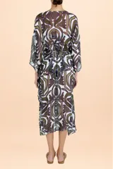 Caftán largo de estilo cover up, confeccionado en tela semitransparente con estampado botánico abstracto en tonos verde oliva y púrpura. Presenta mangas amplias tipo kimono, escote en V y cierre frontal con cordón ajustable en la cintura.