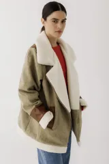 Gamulán de paño en color beige jaspeado con detalles en cuero sintético marrón y forro de corderito sintético blanco. Presenta cierre frontal cruzado, cuello solapa, bolsillos laterales y puños con vuelta.