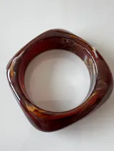 Brazalete rígido de acrílico color marrón oscuro con forma irregular.