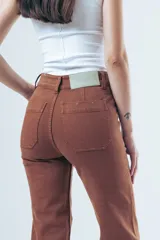 Pantalón de jean tiro alto con corte recto levemente acampanado. Presenta bolsillos delanteros tipo cargo marcados y costuras visibles en color marrón.