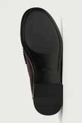 Mocasín de vestir para hombre confeccionado en piel con acabado en gamuza, color marrón. Presenta diseño tipo penny loafer con detalle de antifaz en el empeine, costuras visibles y suela contrastante con un ligero tacón.