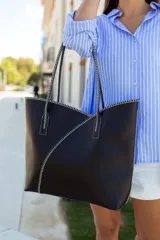 Bolso tipo tote de cuero negro, con costuras decorativas en hilo blanco que forman un diseño geométrico y minimalista. Cuenta con doble asa larga para llevar al hombro.