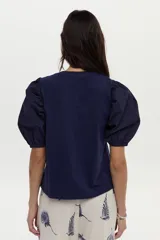Blusa azul marino de algodón, con mangas abullonadas cortas de tela plana y gran bordado de rosa en tono crudo en el pecho.