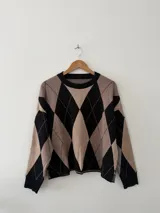 Sweater de tejido bremer con diseño de rombos en colores negro y beige, cuello redondo y mangas largas.