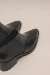 Botín chelsea de cuero vacuno color bordó con acabado charol, punta fina y elástico lateral negro. Posee un taco ancho y bajo de goma.