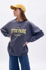 Buzo oversize azul con cuello redondo y estampado frontal en amarillo que dice "London Hyde Park Around The World Global Dreamers".