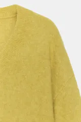 Jersey de punto con mezcla de lana y alpaca, color amarillo mostaza, con cuello en pico y manga larga. Presenta acabados en rib en puños y bajo.